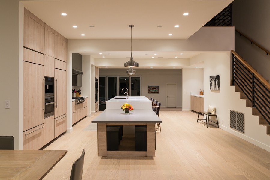 A modern kitchen with recessed ceiling lights, pendant lights over the island, and warm wood cabinetry.