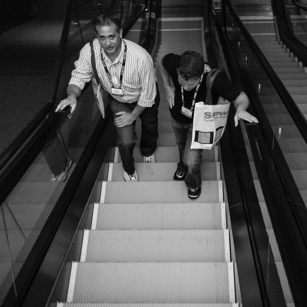 Two men walking up escalator, black and white